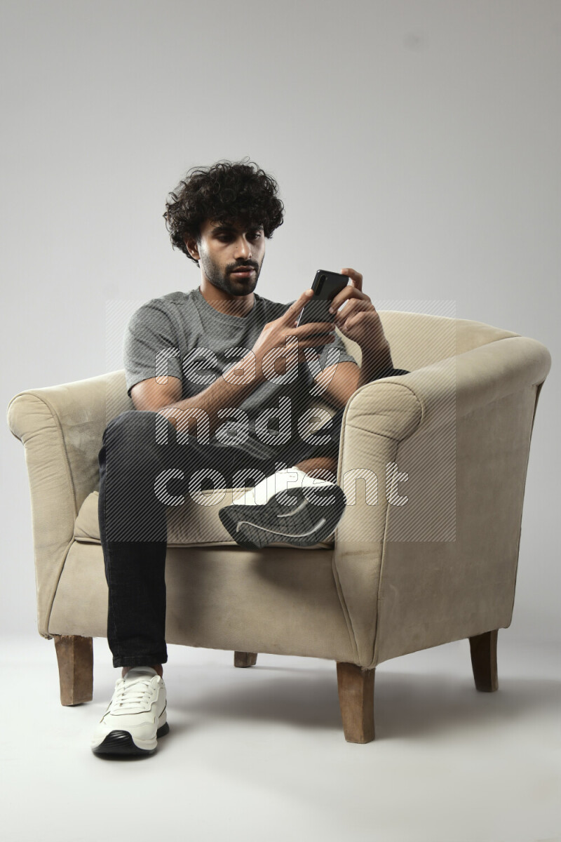 A man wearing casual sitting on a chair browsing on the phone on white background