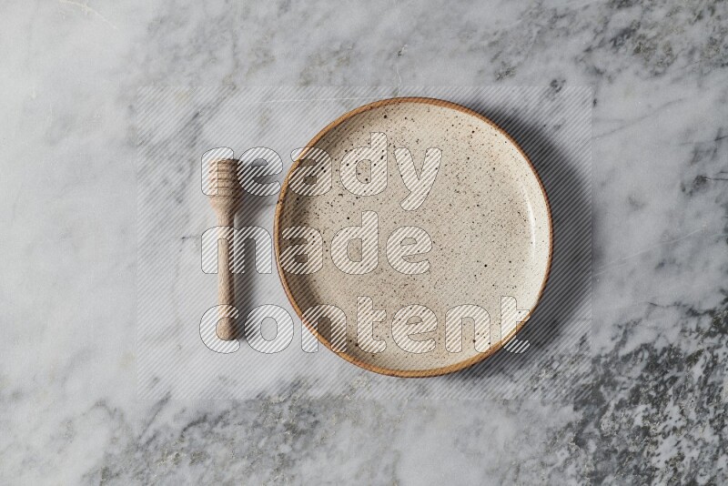 Multicolored pottery plate with wooden honey dipper on the side on grey marble background