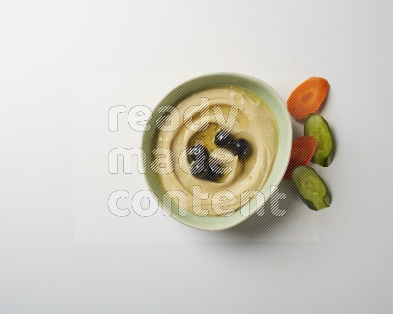 Hummus in a green plate garnished with black olives on a white background