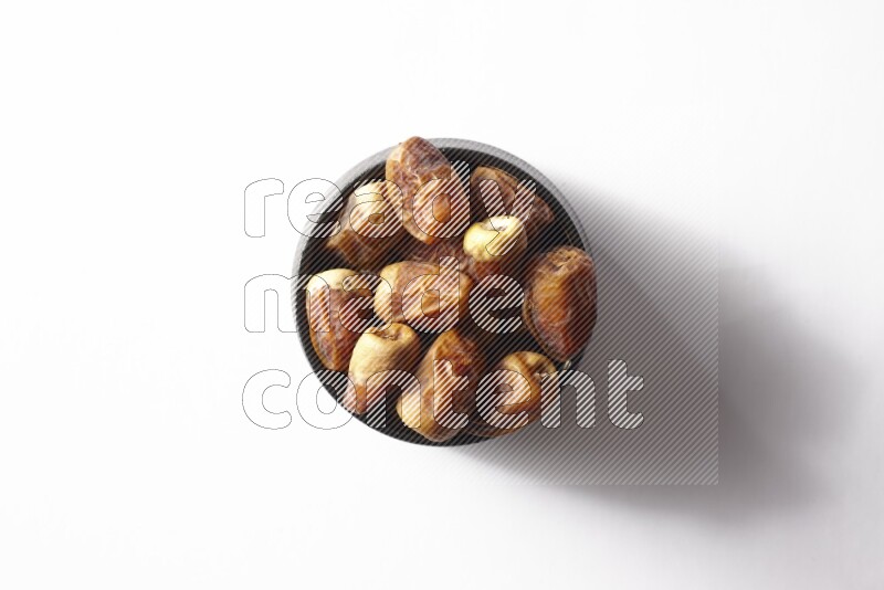 Dates in a black pottery bowl on white background