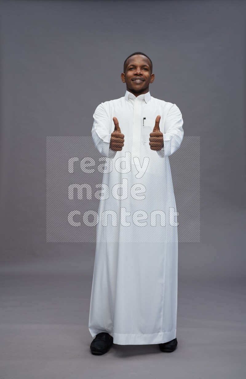 Saudi man wearing thob standing interacting with the camera on gray background