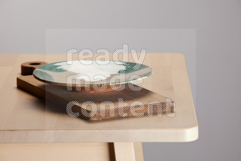 multi-colored pottery Plate placed on a  wooden rectangular cutting board on the edge of wooden table