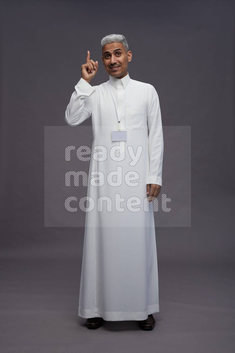 Saudi man wearing thob with neck strap employee badge standing interacting with the camera on gray background