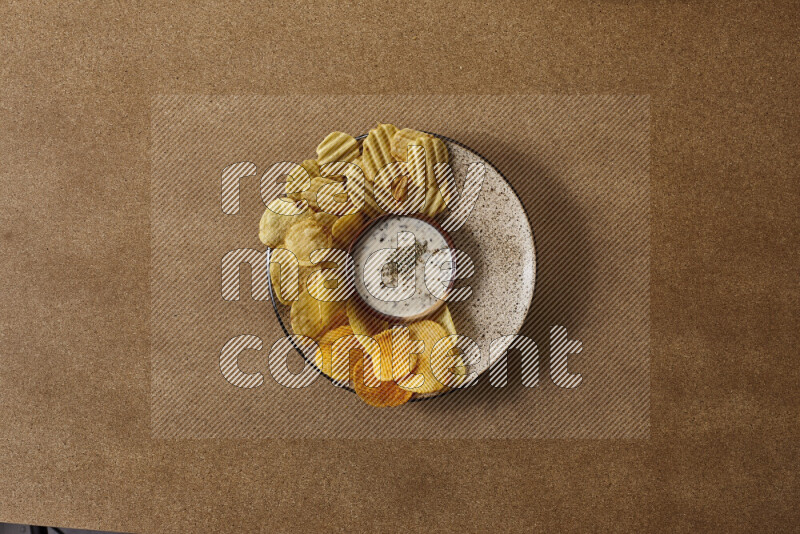 Assorted snacks on a pottery plate with a dipping on brown background