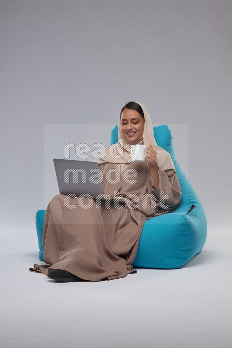 A Saudi woman sitting on a blue beanbag and working on laptop