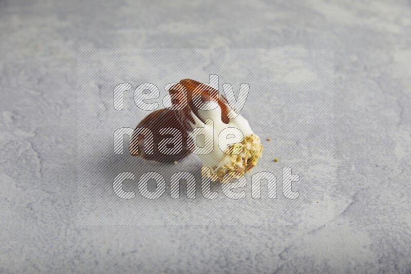 Hazulnut stuffed date covered with white chocolate and crushed peanuts & pistachios on light grey background