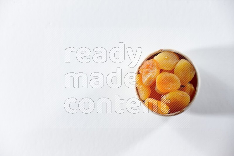 A beige ceramic bowl full of dried apricots on a white background in different angles