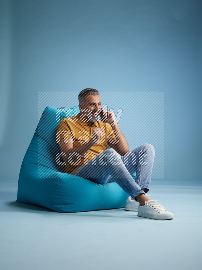A man sitting on a blue beanbag and talking on the phone