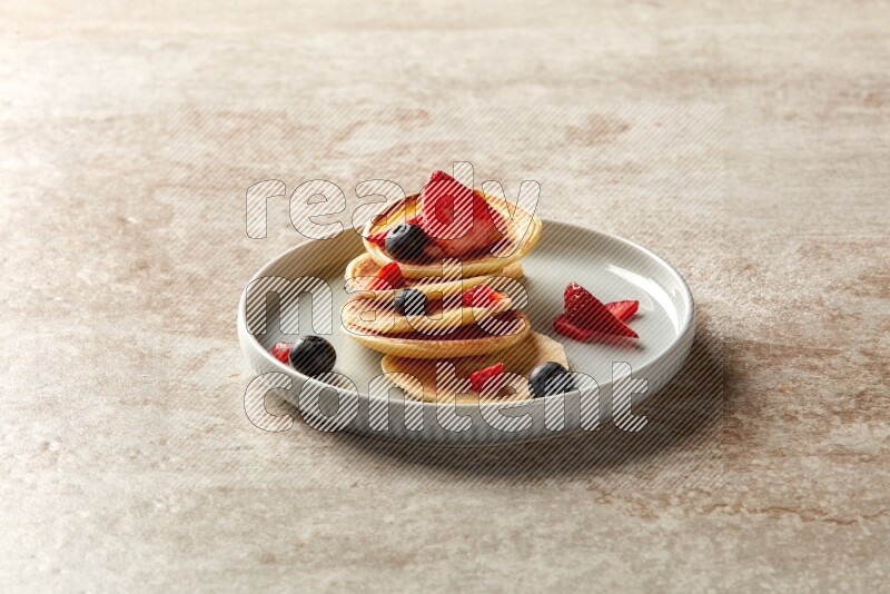 Five stacked mixed berries mini pancakes in a blue plate on beige background