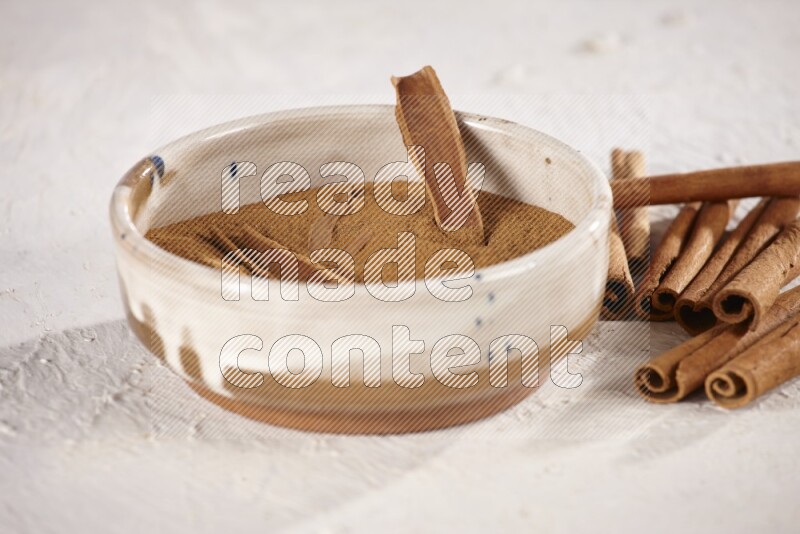 Ceramic bowl full of cinnamon powder with cinnamon sticks on the side on white background