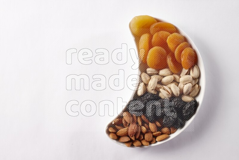 Mixed nuts and dried fruits in a crescent pottery plate on white background