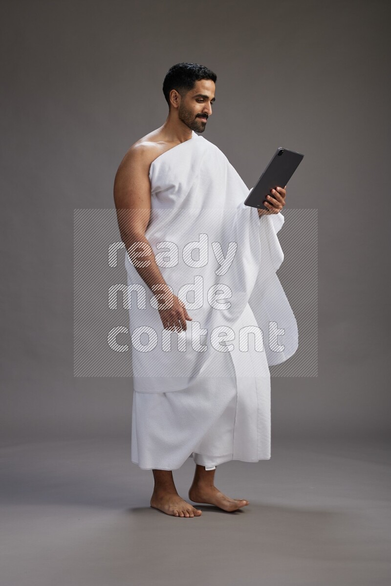 A man wearing Ehram and holding a tablet on gray background