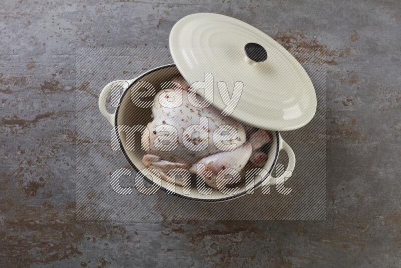 whole raw chicken on in a white ceramic pot direct on a rustic grey background