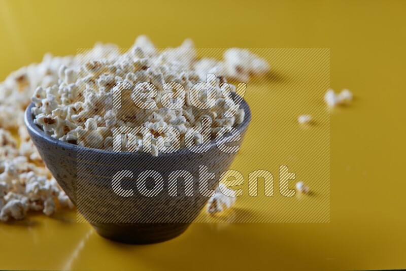 A multicolored pottery bowl full of popcorn with popcorn beside it on a yellow background in different angles
