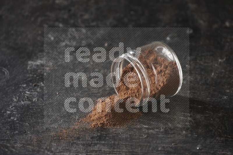 A flipped glass jar full of cloves powder on a textured black flooring