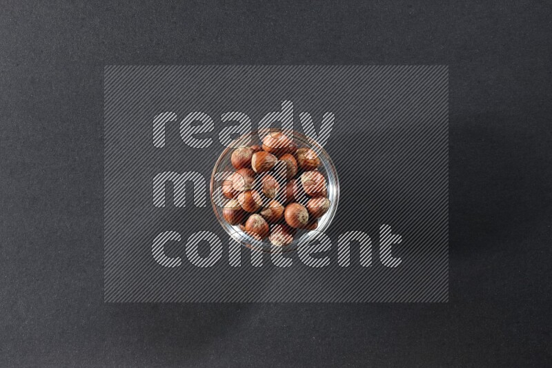 A glass bowl full of hazelnuts on a black background in different angles