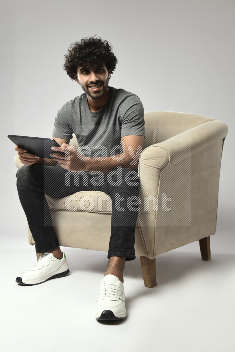 A man wearing casual sitting on a chair gaming on a tablet on white background