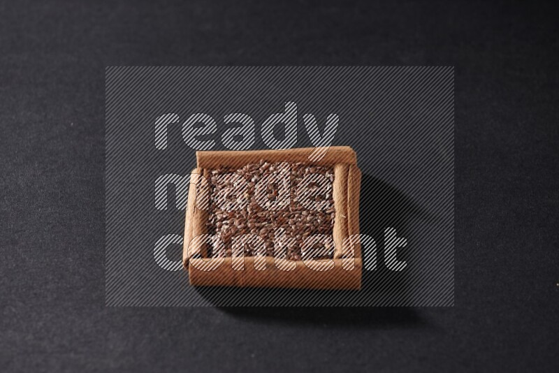 أربعة من أعواد القرفة مكونة شكل مربع بداخلها بذور الكتان علي خلفية سوداء