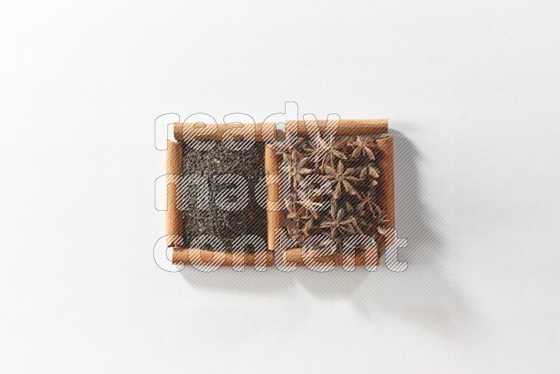 مربعان من أعواد القرفة ممتلئان باليانسون النجمي والشاي الأسود علي خلفية بيضاء