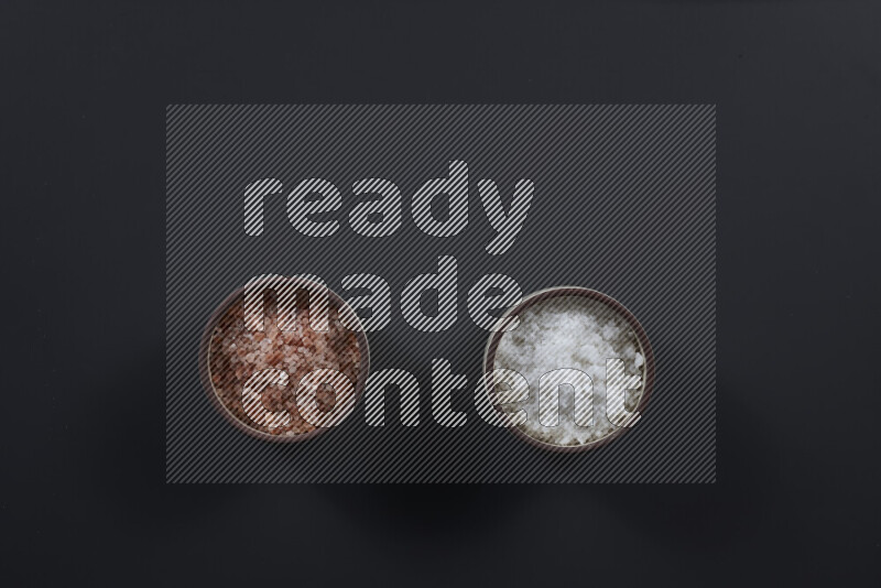 2 pottery bowls one is filled with himalayan salt and the other with white salt on black background