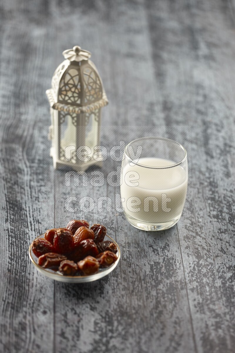 A white lantern with different drinks, dates, nuts, prayer beads and quran on grey wooden background