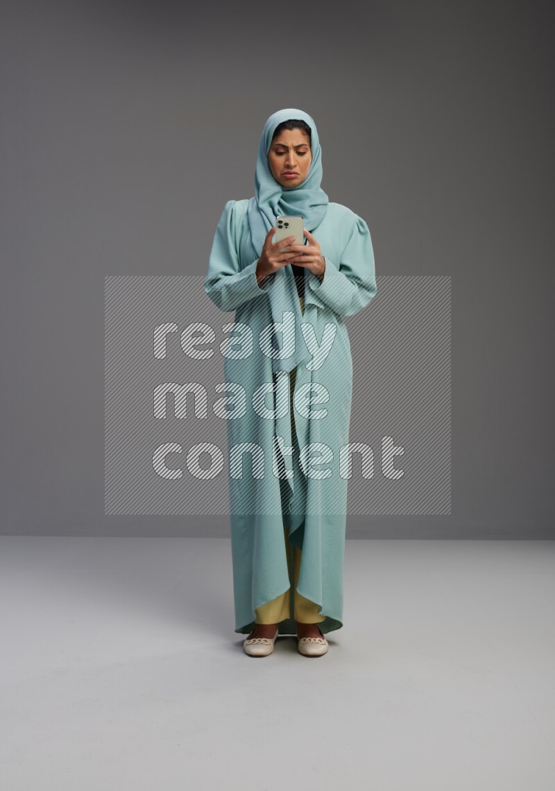 Saudi Woman wearing Abaya standing texting on phone on Gray background