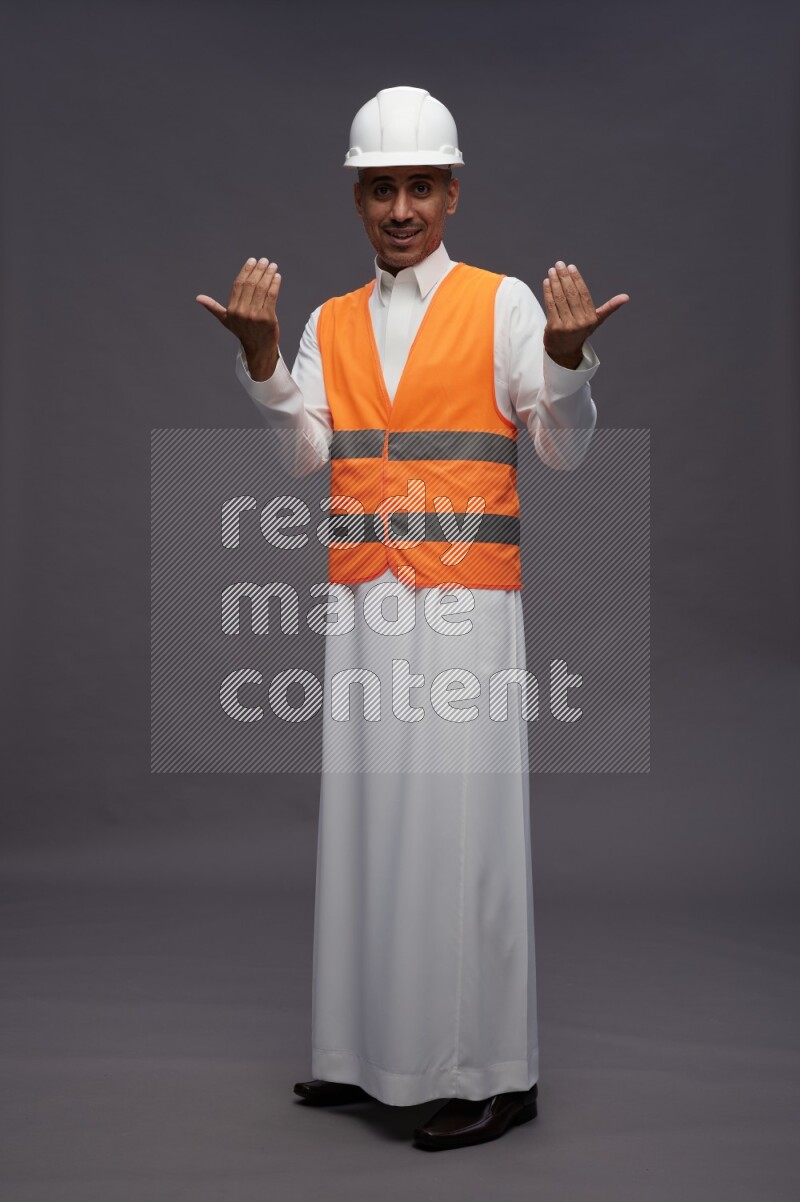 Saudi man wearing thob with engineer vest standing interacting with the camera on gray background