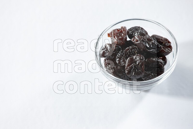 A glass bowl full of dried plums on a white background in different angles