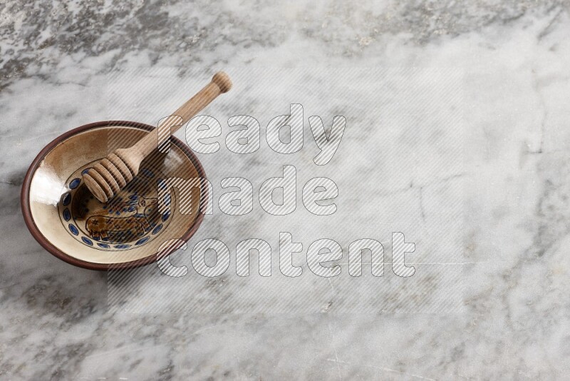 Decorative pottery plate with wooden honey dipper in it on grey marble background