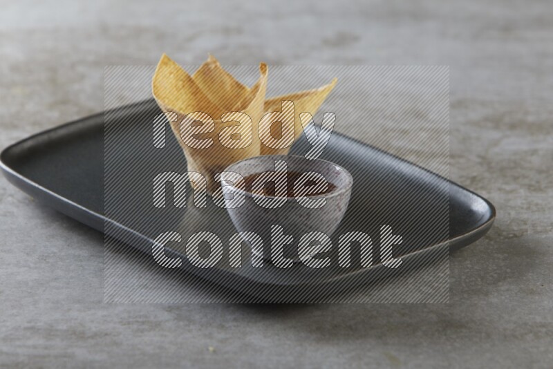 wonton cups with soy sauce ramkin on rectangle dark grey ceramic plate on grey textured counter top