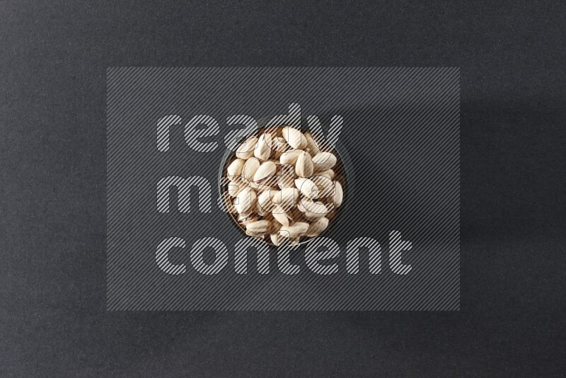 A black pottery bowl full of pistachios on a black background in different angles