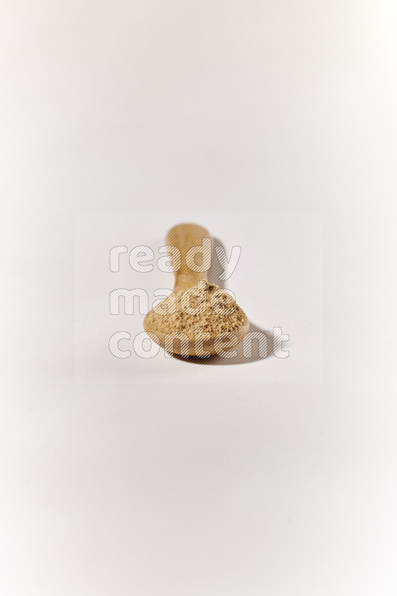 A wooden spoon full of ground ginger powder on white background