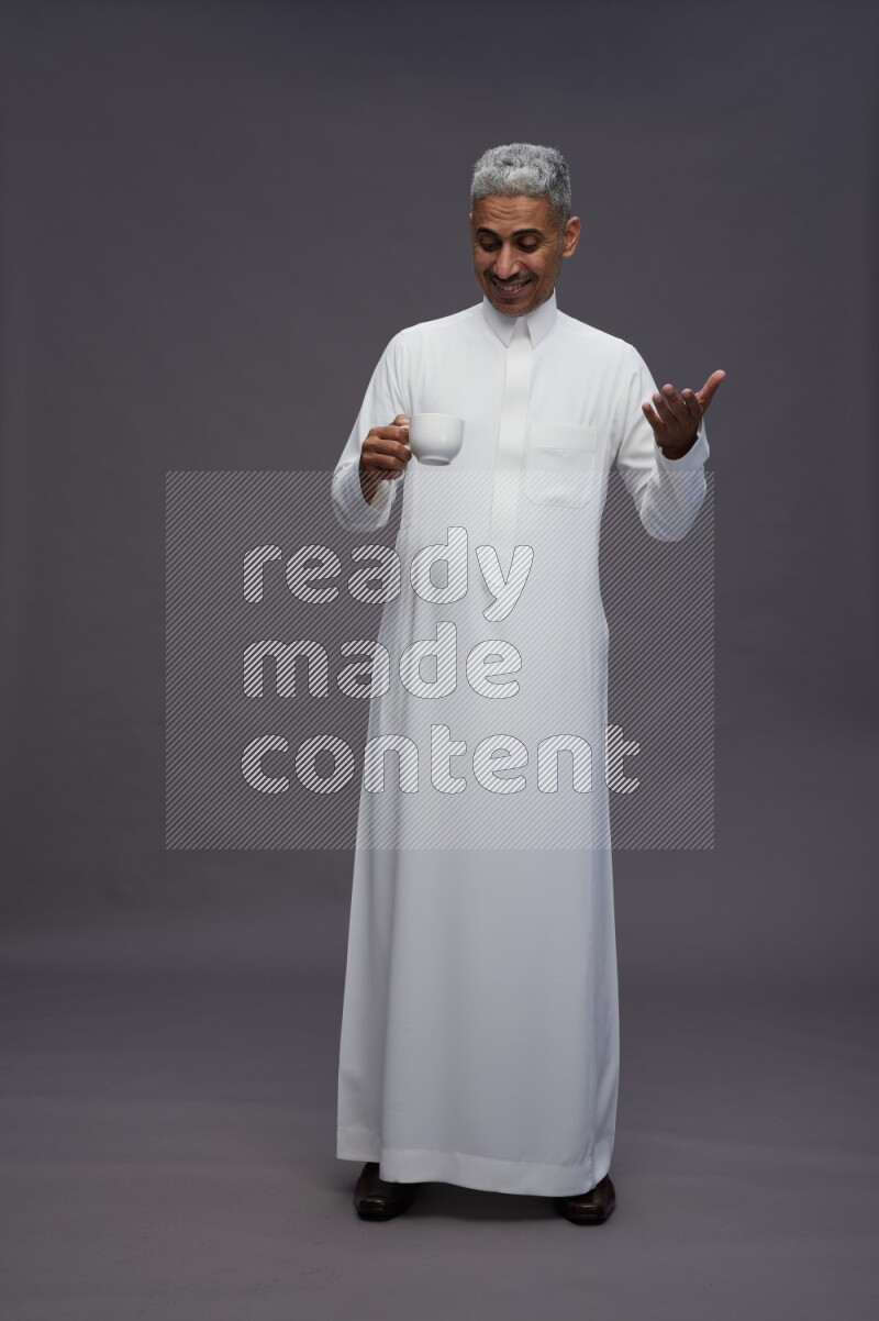 Saudi man wearing thob standing holding mug on gray background