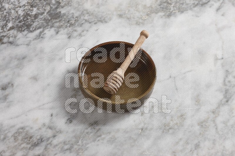 Multicolored pottery oven plate with wooden honey dipper in it on grey marble background
