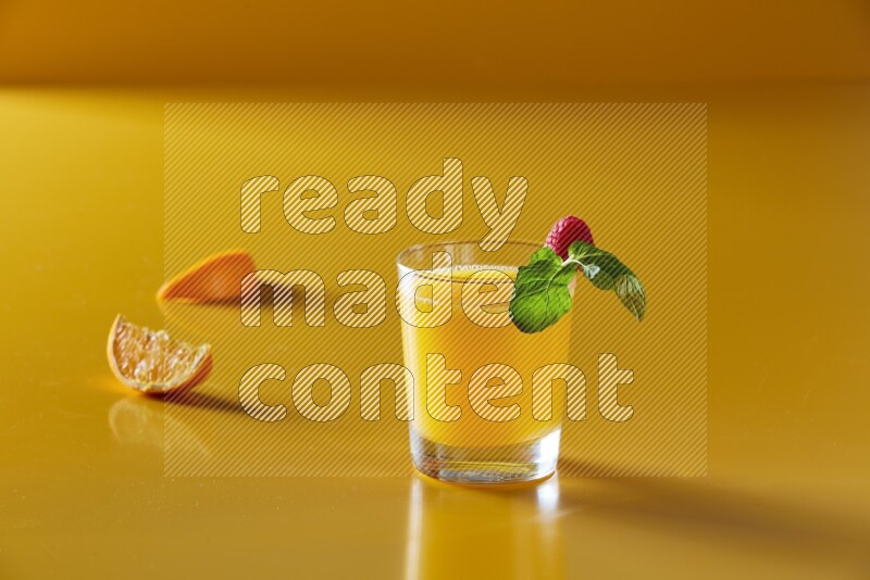 glass of orange juice with berry & mint on yellow background