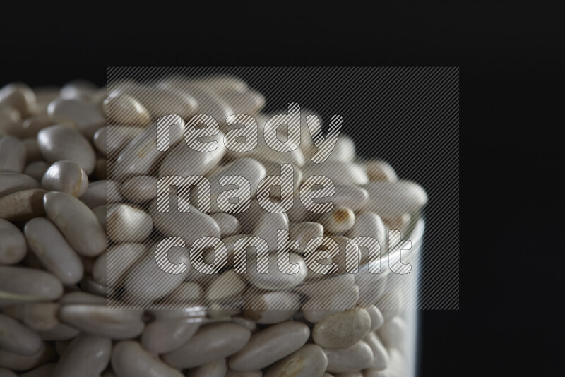 White beans in a glass jar on black background