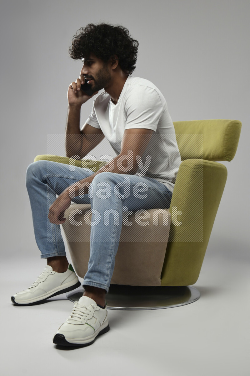 A man wearing casual sitting on a chair talking on the phone on white background