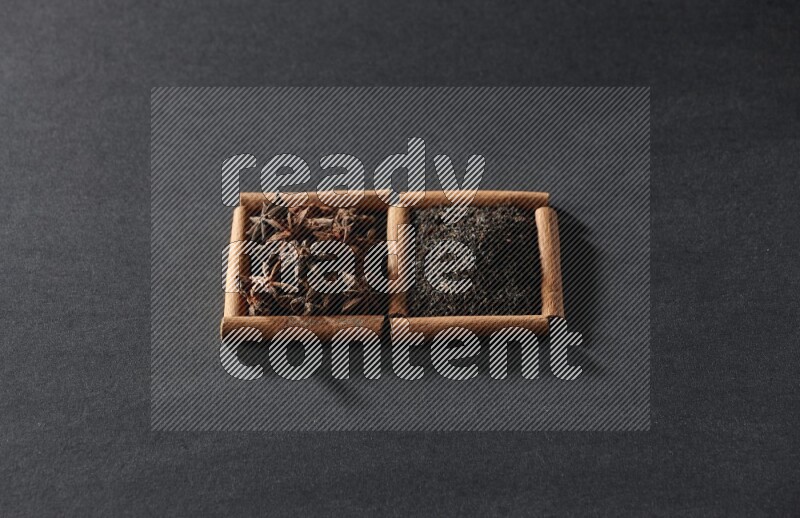 مربعان من أعواد القرفة ممتلئان باليانسون النجمي والشاي الأسود علي خلفية سوداء