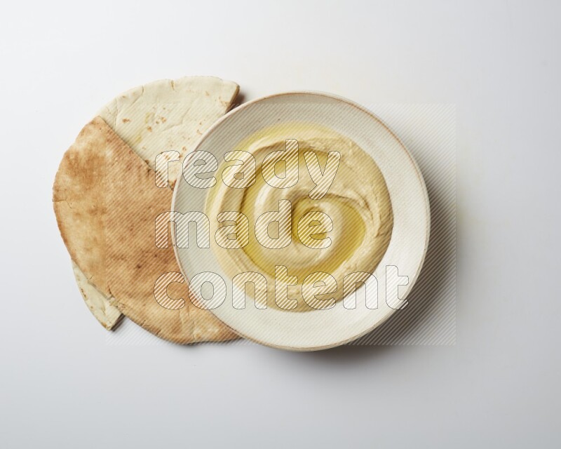 Hummus in a pottry plate garnished with olive oil on a white background