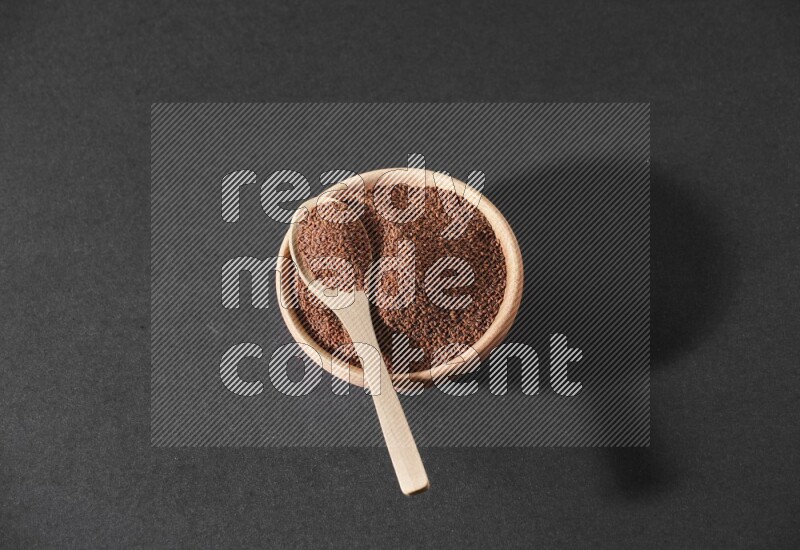 A wooden bowl full of garden cress seeds and a wooden spoon full of the seeds on it on a black flooring