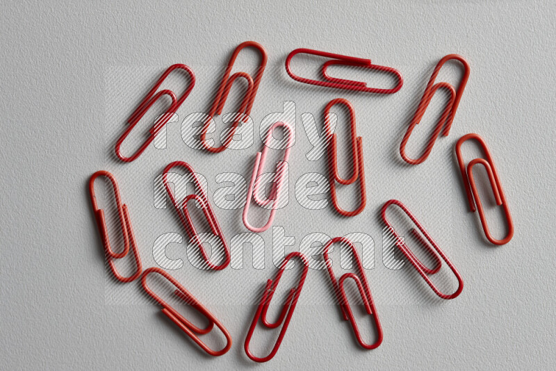 A bunch of red paper clips with a different colored paper clip in the center on grey background