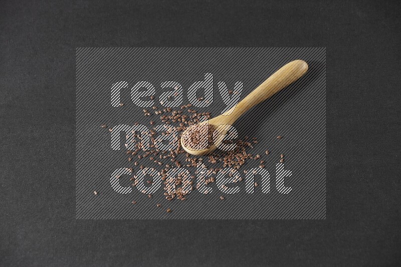 ملعقة خشبية ممتلئة بحبوب بذر الكتان وبعض البذور متناثرة علي خلفية سوداء