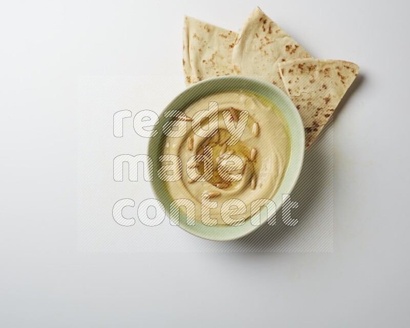 Hummus in a green plate garnished with pine nuts on a white background