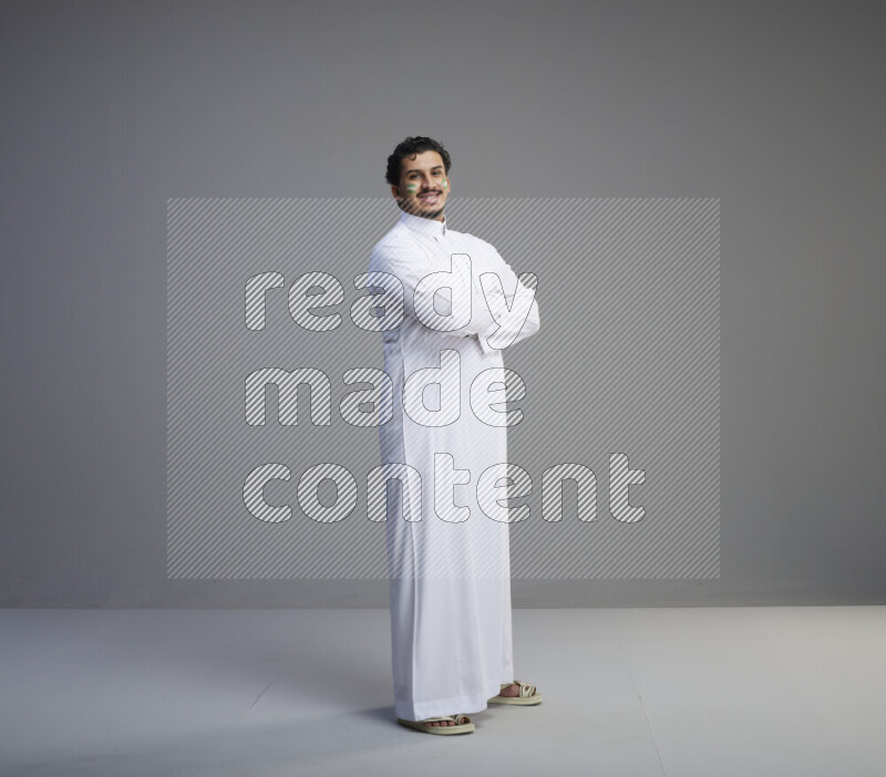 A Saudi man standing wearing thob with face painting interacting with the camera on gray background