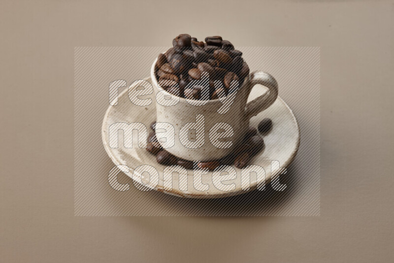 A beige pottery cup full of roasted coffee beans on beige background