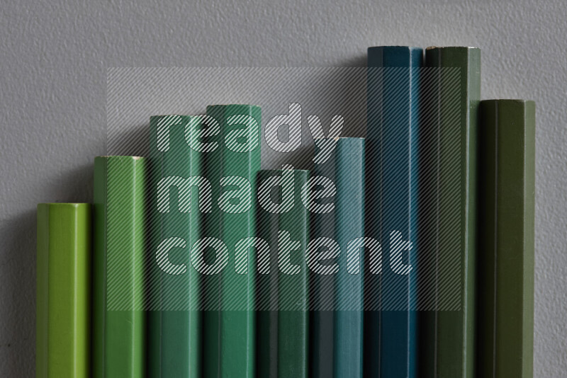 مجموعة من أقلام الرصاص الملونة مرتبة لتعرض تدرجا من الألوان الخضراء علي خلفية رمادية