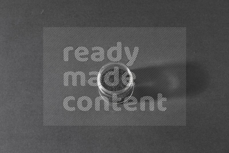 A glass jar full of black seeds on a black flooring