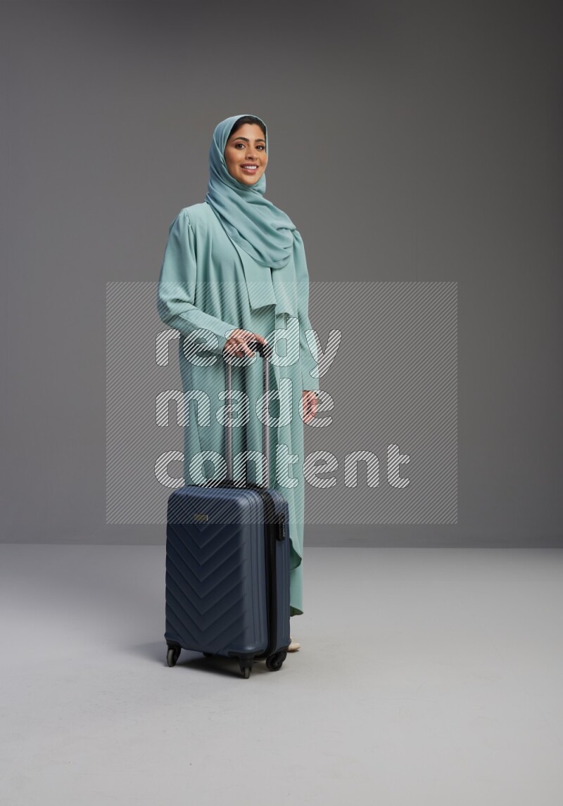 Saudi Woman wearing Abaya standing holding Travel bag on Gray background