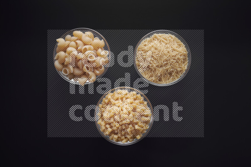 Different pasta types in glass bowls on black background