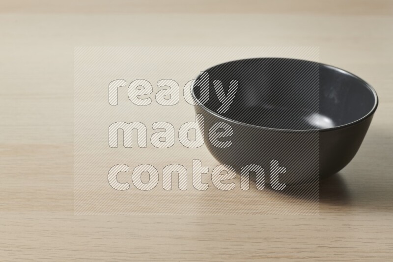 A black ceramic bowl on light wooden background